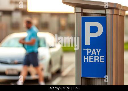 Parkuhr mit Text bezahlen und verschwommenes Fahrzeug und Mensch im Hintergrund. Kostenpflichtige Parkplätze mit Maschine gegen Bezahlung. Stockfoto