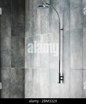 Fließendes Wasser aus dem Duschkopf in einer grauen Dusche im Badezimmer Stockfoto