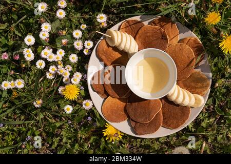 Pfannkuchen mit Honig und Bananen auf dem grünen Gras gekrönt Stockfoto