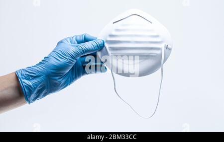 Hand tragen schützende chirurgische Handschuh hält Gesichtsmaske. Sicherheitsmaßnahmen zur Bekämpfung der Virusepidemie. Stockfoto