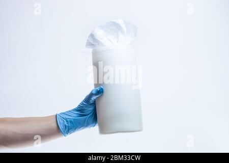 Die Hand der Frau, die chirurgische Schutzhandschuhe trägt, hält einen Plastikspender mit feuchten Reinigungstüchern für Desinfektionsmittel. Produkte, die Keime und Viren töten Stockfoto