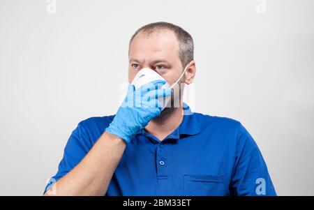 Porträt des Mannes in seiner Mitte 30er Jahre mit Schutzmaske und OP-Maske auf weiß ausgestattet. Mitarbeiter im Gesundheitswesen hält die Hand über die Gesichtsmaske. Stockfoto