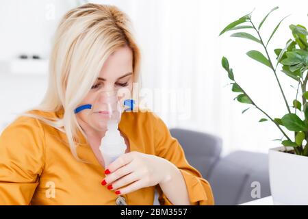 Krank schöne weibliche hält Nasenmaske mit Atembeschwerden im Krankenhauszimmer. Frau Patient Inhalationstherapie durch die Maske von Inhalator mit weich Stockfoto