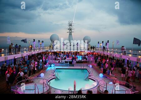 Eine farbenfrohe Party und Feier, die in der Abenddämmerung auf dem Hauptdeck eines Luxuskreuzfahrtschiffes stattfindet Stockfoto