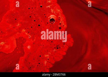 Verschüttete rote Farbe mit Blasen und Streifen. Nahaufnahme des roten Punktes. Abstrakter natürlicher Hintergrund Stockfoto