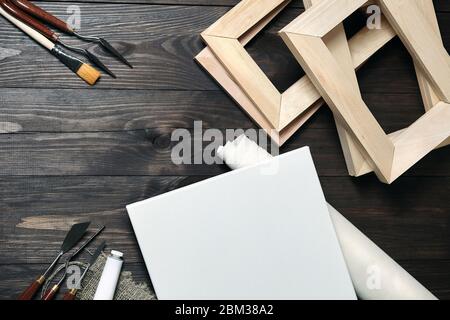 Eine weiße leere Leinwand, Palettenmesser, synthetischer Pinsel, eine Tube mit Öl- oder Acrylfarbe und Tragbahren auf einem braunen Holzhintergrund. Oben vi Stockfoto