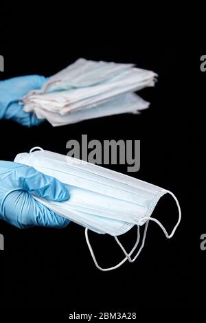Gesichtsmasken, medizinische Sanitär-OP-Einwegmasken in der Hand in blauen Handschuh, isoliert auf schwarzem Hintergrund Stockfoto
