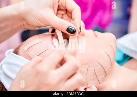 Kinesiotaping. Kosmetikerin klebt Klebeband auf dem Gesicht einer Frau. Physiotherapie und Kosmetologie Verfahren. Methode der nicht-chirurgischen Hautverjüngung. Fa Stockfoto