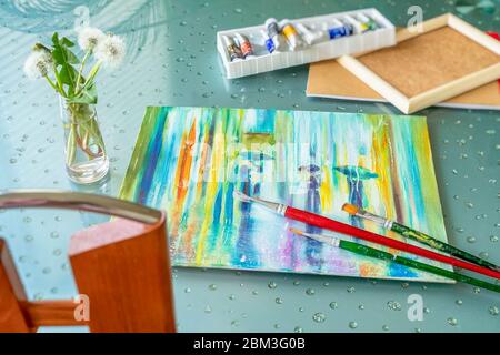Tisch mit liegendem Ölgemälde auf Leinwand, Schachtel mit Farben in Röhren, Pinsel und Strauß flauschigen Löwenzahn. Romantisches Konzept von Frühling, Freizeit Stockfoto
