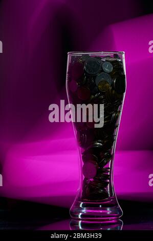 Bierglas mit Münzen auf schwarzem Hintergrund mit Hintergrundbeleuchtung gefüllt Stockfoto