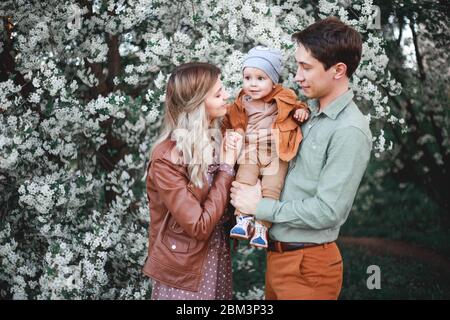 Glückliche Eltern Mama und Papa, Sohn stehen im Garten im Frühjahr vor dem Hintergrund der blühenden Apfel und Kirschbäume Stockfoto