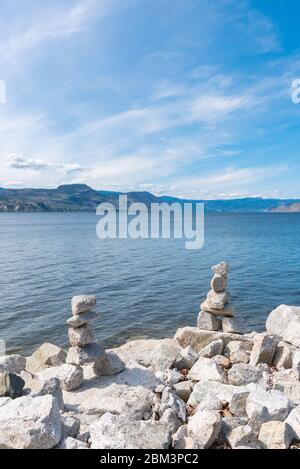 Blick auf den Okanagan Lake und die Berge mit blauem Himmel und ausgeglichenen Felsen am Seeufer Stockfoto