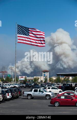 Bastrop, Texas, USA, September 5 2011: Die amerikanische Flagge fliegt über einem Parkplatz, während der Rauch eines unkontrollierten Wildfeuers im Hintergrund in die Höhe schießt. Nach Schätzungen der Behörden wird es mehrere Tage dauern, das Feuer unter Kontrolle zu bringen; es hat bereits Tausende Hektar von timberland und Busch verbrannt. ©Bob Daemmrich Stockfoto