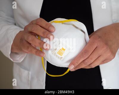 Latina Ärztin trägt weißes Fell und hält eine 3M N-95 Gesichtsmaske in den Händen. Stockfoto