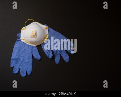 Eine 3M N-95 Gesichtsmaske und blaue Einweg-Handschuhe auf schwarzem Hintergrund. Fotografieren mit geringer Schärfentiefe. Stockfoto