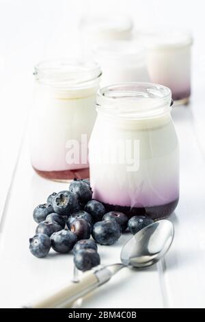 Weißer fruchtiger Joghurt im Glas und Heidelbeeren auf weißem Tisch. Stockfoto