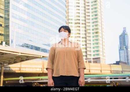 Übergewichtige asiatische Frau mit Maske denken an Skywalk Brücke Stockfoto