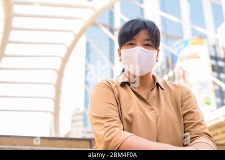 Übergewichtige asiatische Frau mit Maske sitzt in der Stadt Stockfoto