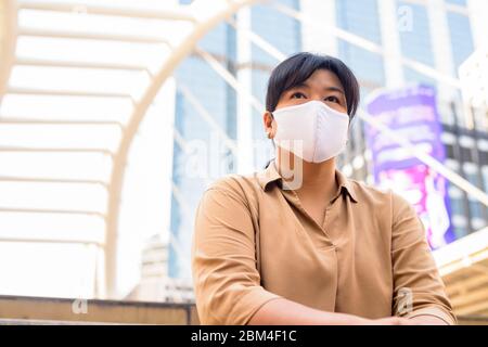 Übergewichtige asiatische Frau mit Maske Denken, während in der Stadt sitzen Stockfoto