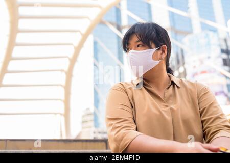 Übergewichtige asiatische Frau mit Maske Denken, während in der Stadt sitzen Stockfoto