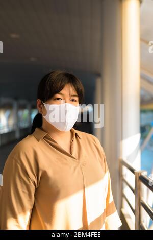 Übergewichtige asiatische Frau mit Maske Denken an Fußgängerbrücke in der Stadt Stockfoto