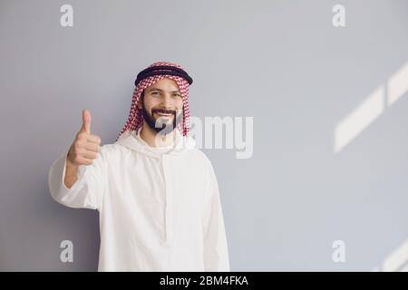 Attraktive lächelnde araber zeigt Daumen auf grauem Hintergrund für Text. Stockfoto