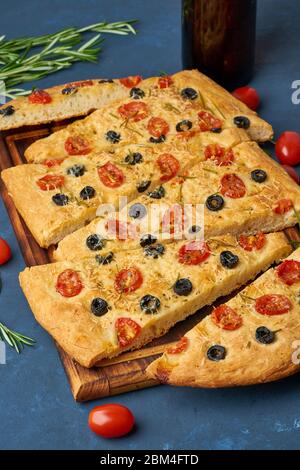 Focaccia, Pizza, italienisches Fladenbrot mit Tomaten, Oliven und Rosmarin. Dunkelblauer Hintergrund, Stockfoto