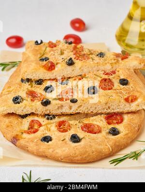 Focaccia, Pizza, gehacktes italienisches Fladenbrot mit Tomaten, Oliven und Rosmarin. Vertikal, Stockfoto