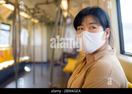 Übergewichtige asiatische Frau mit Maske Denken während mit Abstand im Zug sitzen Stockfoto