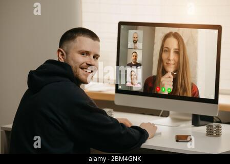 Remote-Arbeit. Eine Rückansicht eines Mannes während eines Videoanrufs mit seinen Kollegen auf dem Desktop-Computer. Ein Kollege lenkte ab und lächelte von einem Online-Brief Stockfoto