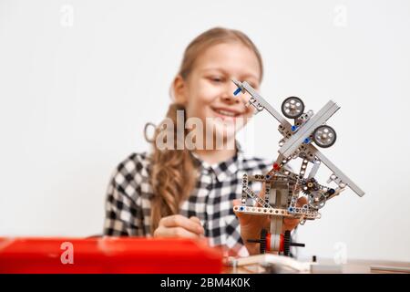 Selektive Fokus von interessanten Roboter in den Händen von jungen lächelnden Mädchen am Tisch sitzen. Nahaufnahme des Fahrzeugs mit Baukasten für Kinder gemacht. Konzept der naturwissenschaftlichen Ingenieurskunst. Stockfoto