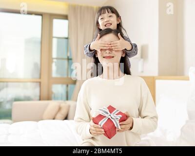 Happy Little Asian Girl Mutter ein Geschenk und bedeckt Mutter die Augen mit Händen Stockfoto