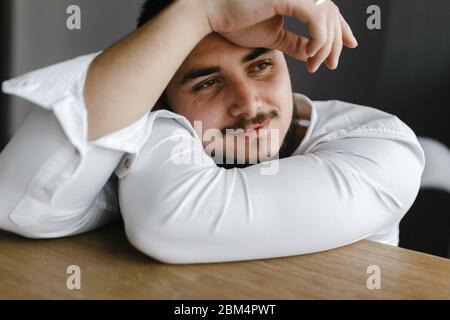 Lächelnder Brünette Mann im weißen Hemd, der zur Seite schaut. Bleib zu Hause. Mannporträt Stockfoto