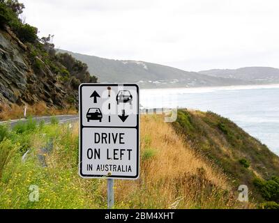 Australische Verkehrszeichen, um die Fahrer daran zu erinnern, auf der linken Straßenseite zu fahren. Mit Ozean im Hintergrund. Stockfoto