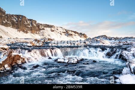 Schnell fließender Wasserfall im Hof-Gebiet im Süden Islands. Schnelle Belichtung bei eingefrorenen Bewegungen. Panoramablick mit klarem blauen Himmel Hintergrund. Stockfoto