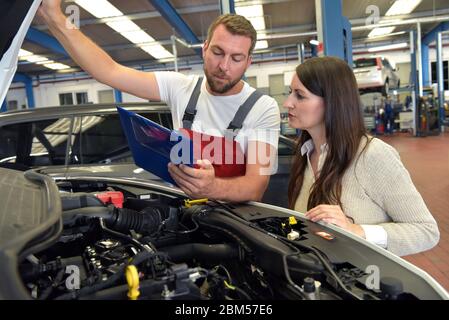 Kundendienst: Kfz-Mechaniker und Kunde besprechen die Reparatur eines Fahrzeugs vor Ort Stockfoto