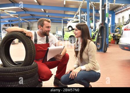 Mechaniker und Kunde sprechen in einer Garage miteinander - Reifen vom Auto wechseln Stockfoto