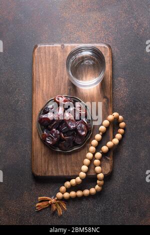 Ramadan. Hölzerne Gebetskugeln und Datteln in Schale auf braun. Blick von oben. Vertikales Format. Eid Mubarak. Religiöse Tradition. Stockfoto