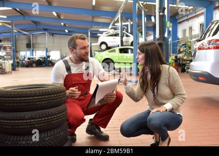 Mechaniker und Kunde sprechen in einer Garage miteinander - Reifen vom Auto wechseln Stockfoto