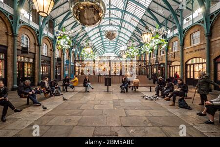 Covent Garden, London. Touristen und Käufer ruhen sich von ihren Weihnachtseinkäufen in einem Sitzbereich im Zentrum von Londons Covent Garden aus. Stockfoto