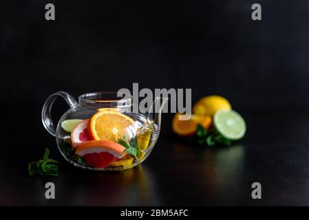 Heißer Früchtetee mit Zitrone, Minze, Orange, Limette und Grapefruit in einer schönen Glas-Teekanne Stockfoto