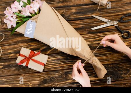 Cropped Ansicht der Frau berühren Jute Garn Seil auf rosa Blumen in Papier in der Nähe Geschenkbox und Schere, Muttertag Konzept gewickelt Stockfoto