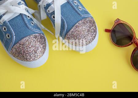 Kinder-Textil-Spitze-Sneakers. Mädchen Schuhe auf gelbem Hintergrund.Mode Kinderschuhe.Smart lässige modische Denim und glänzende Schuhe. Sonnenbrillen und Stockfoto