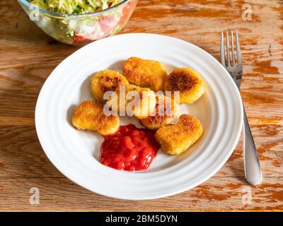 Portion gebratene Chicken Nuggets aus gefrorenem Produkt (frittiertes paniertes Hühnerfleisch) mit Tomatenketchup auf weißem Teller und Salat aus frischem vegetab Stockfoto