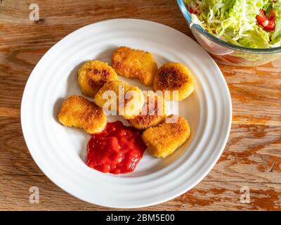 Draufsicht auf gebratene Chicken Nuggets aus gefrorenem Produkt (frittiertes paniertes Hühnerfleisch) mit Tomatenketchup auf weißem Teller und Salat aus frischem Gemüse Stockfoto