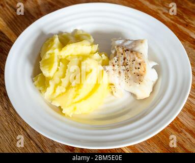 Gekochter Kabeljaufisch mit Kartoffelpüree auf weißem Teller auf altem Holztisch in der heimischen Küche Stockfoto