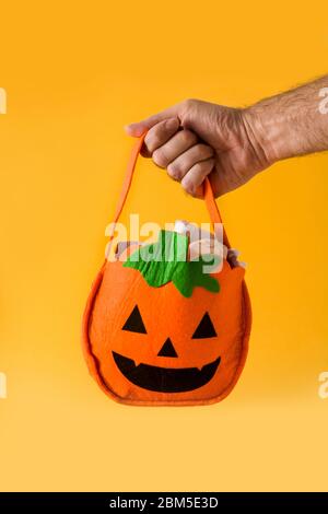 Hand hält Halloween Kürbis Tasche mit Süßigkeiten innen isoliert auf gelbem Hintergrund Stockfoto