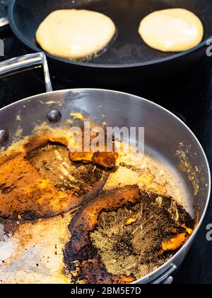 Stahlpfanne mit Kruste von Lebensmitteln verbrannt, während Pfannkuchen auf Elektroherd in der Küche zu Hause braten Stockfoto