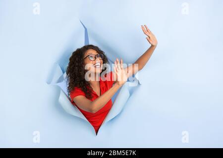 Begrüßung, anhalten. Fröhliche afroamerikanische Frau in zerrissenem blauem Papierhintergrund, emotional, ausdrucksstark. Brechen an, brechen durchnher. Konzept der menschlichen Emotionen, Gesichtsausdruck, Verkauf, Anzeige. Stockfoto