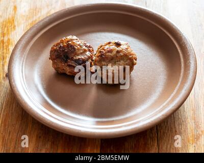 Zwei gebratene russische Kotleta (panierte Fleischbällchen) auf Keramikplatte auf alten Holztisch in der heimischen Küche Stockfoto